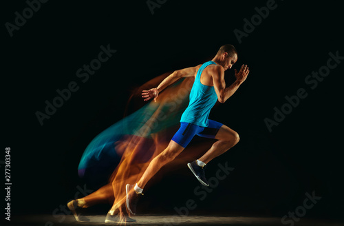 Professional male runner training isolated on black studio background in mixed light. Man in sportsuit practicing in run or jogging. Healthy lifestyle, sport, workout, motion and action concept.