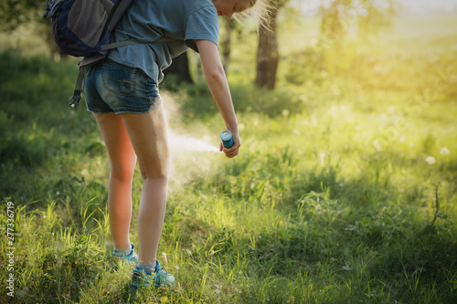 Hiker applying mosquito repellent on the leg skin in the forest.