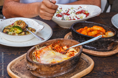 National Montenegrin food. Salty pancakes with meat and cheese in a cast-iron pot, baked vegetables and sopska salata on the table in the restaurant.