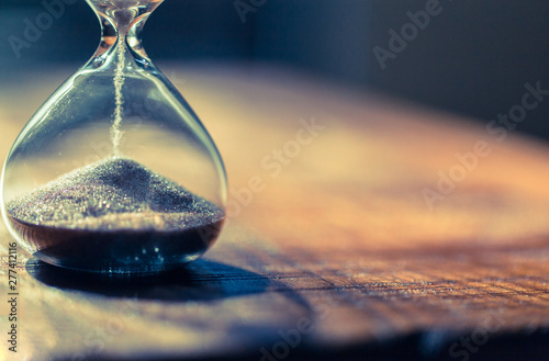 Sand running through the bulbs of an hourglass measuring the passing time in a countdown to a deadline with copy space.