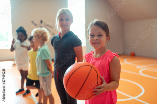 Little schoolgirl with a basketball standing near her classmates.