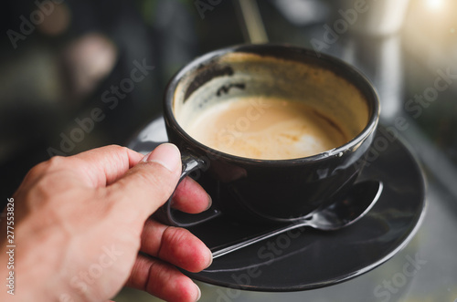 close up hand holding modern hot black coffee the cappuccino on dark background with coffee bubble foam pattern and texture in black cup looking and feel so delicious on glasses table in coffee shop.