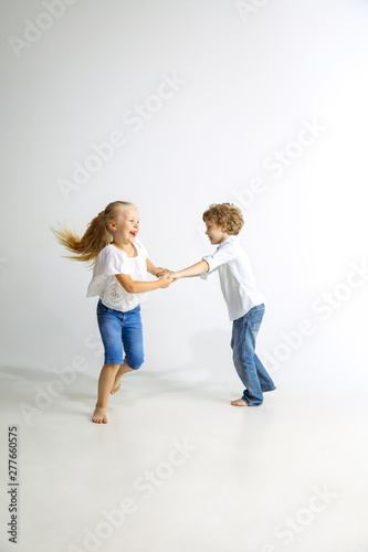 Boy and girl, best friends or brother and sister having fun. Little caucasian models in jeans playing together on white studio background. Childhood, education, holidays or homework concept.