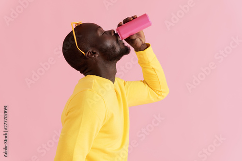 Drink. Black man drinking soft drink on pink background portrait