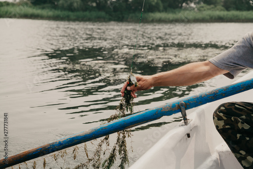 Fisherman removes algae from fishing rod on boat