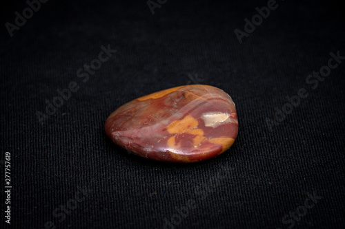 Red gemstone with colorful structure in many tones formed under high pressure found in river
