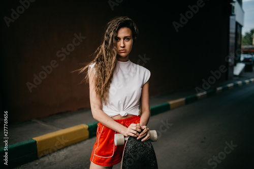 Beautiful skater woman wearing red shorts riding on her longboard in the sunset city