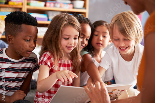 Group Of Elementary School Pupils Sitting On Floor Listening To Female Teacher Read Story