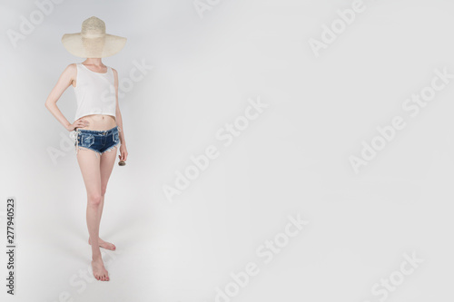the girl in shorts and hat covering her face staying and holding sunglasses on white background isolated