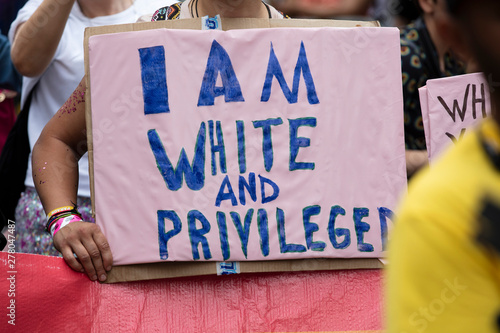 A person holding an I am white and privileged banner at a gay pride event