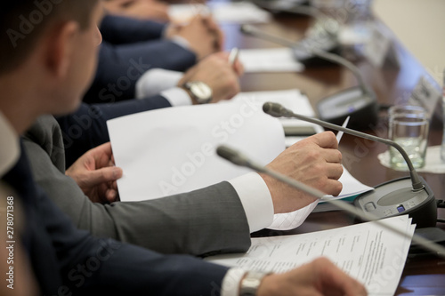 One of politician sitting by table with his hands over document during political summit or conference