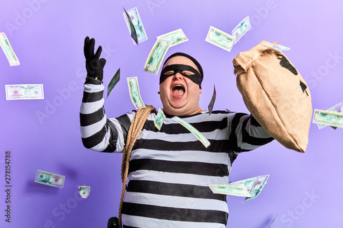 happy cheerful thief enjoying stolen money. isolated blue background studio shot. emotion and feeling