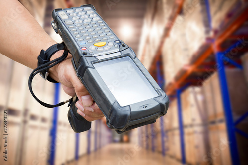 close up hand of worker holding barcode scanner with warehouse background.