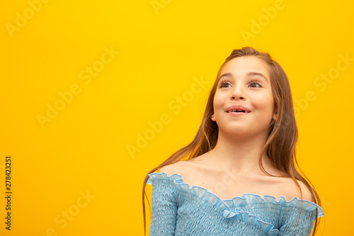 Beautiful female half-length portrait isolated on yellow studio background. Little emotional Brazilian girl. Facial expression, human emotions, advertising concept. Thinking, looking up.