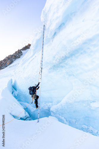 Alpinist mountaineer climb ladder over ice crevasse.