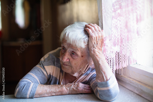 Elderly woman sits sadly near the window.