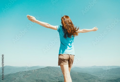 Woman standing with raised arms on background of sky and mountains.