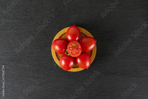 Group of five whole one half of fresh red tomato cherry on a bamboo plate flatlay on grey stone