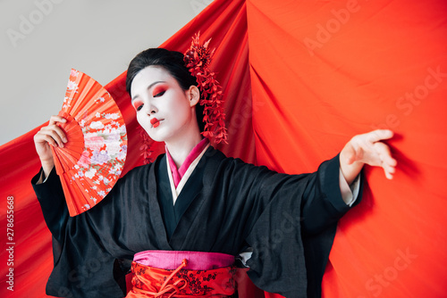 beautiful geisha in black kimono with hand fan and red cloth on background dancing isolated on white