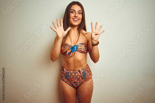 Young beautiful woman on vacation wearing bikini standing over isolated white background showing and pointing up with fingers number nine while smiling confident and happy.