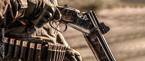 Hunter man. Hunting period. Male with a gun, rifle. Man is charging a hunting rifle. Male hunter in ready to hunt. Closeup. The man is on the hunt, sport