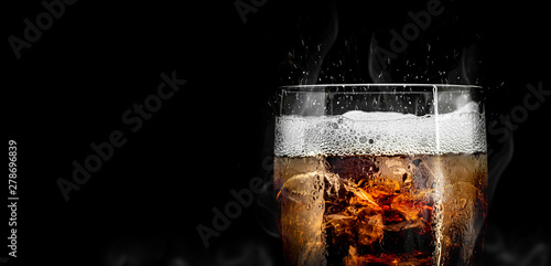 Soft drink glass with ice splash on cool smoke background. Cola glass with summer refreshment.
