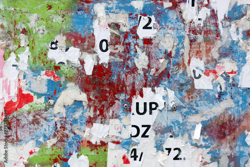 Grungy flat wall surface covered with pealed paper and red, green and blue spray paint 