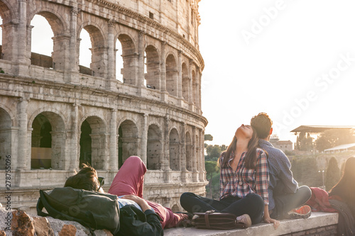 Three happy young friends sitting and lying in front of colosseum in rome