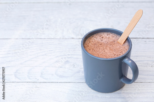 Hot chocolate in a blue-grey ceramic mug with wooden stirrer isolated on white painted wood. Space for text.