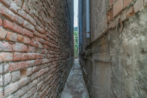 The narrow space between the two brick houses, at the end of the gap with the trees