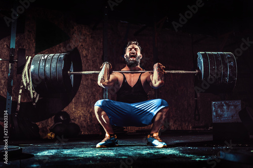 Muscular bearded tattoed fitness man doing deadlift a barbell over his head in modern fitness center. Functional training. Snatch exercise