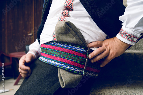 Midsection of man wearing serbian national folk costume with traditional hat on his waist sitting outdoors