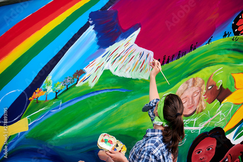 Frau malt Friedenstaube auf bunte Wand