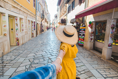 follow me concept. woman in yellow sundress in straw hat walking forward by small resort city street holding man hand