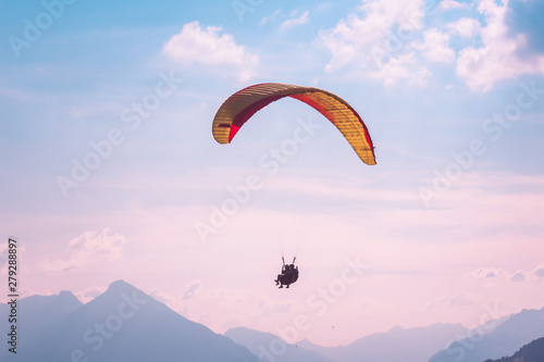 Paragliding in tandem in Interlaken, Switzerland. Photographed in pink sunset light. Silhouettes of paragliders and Swiss Alps. Adventure lifestyle. Extreme sports. Adrenaline activity