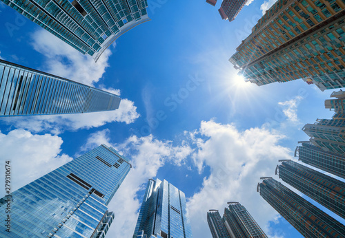 Looking up at modern office buildings. Financial district and business centers in smart city for technology background. Skyscraper and high-rise buildings in Hong Kong at noon with blue sky.