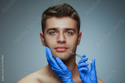 Close-up portrait of young man isolated on grey studio background. Filling botox surgery procedure. Concept of men's health and beauty, cosmetology, self-care, body and skin care. Anti-aging.