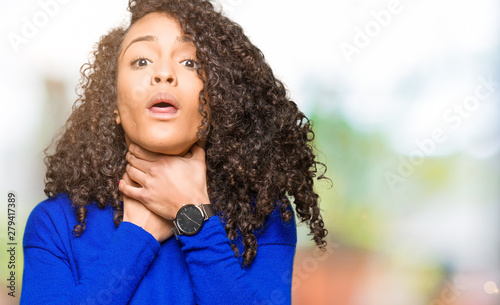 Young beautiful woman with curly hair wearing winter sweater shouting and suffocate because painful strangle. Health problem. Asphyxiate and suicide concept.