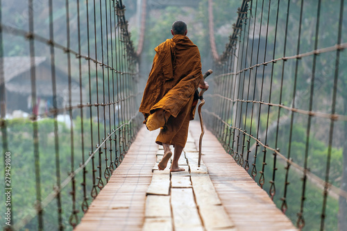 monk is walking on a wooden bridge.