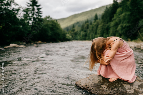 Young depressive girl sitting at stone in the river.