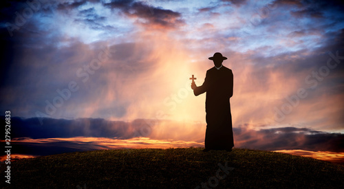 pastor - priest on the hill at sunset with the cross