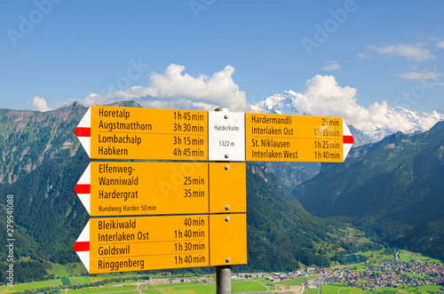 Yellow tourist sign on the top of Harder Kulm, Interlaken, Switzerland. The information sign specifies the directions and distances. Amazing summer Alpine landscape in background. Swiss Alps, tourism