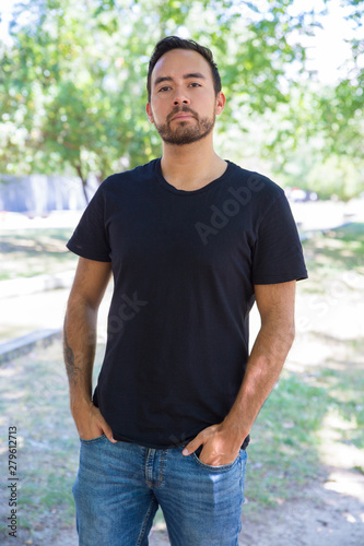 Confident man standing with hands in pockets. Handsome bearded young man in black t-shirt standing outdoor. Confidence concept