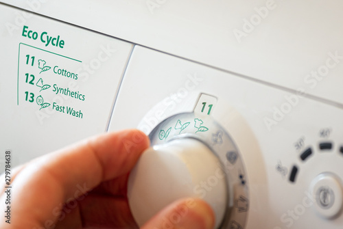 Close up of hand selecting green eco cycle programme on washing machine.