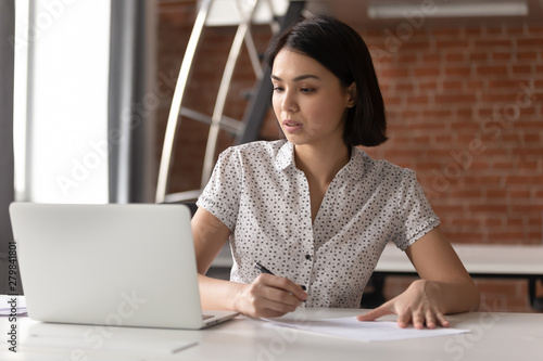 Focused asian business woman working looking at laptop making notes