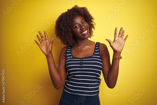 Young african afro woman wearing striped t-shirt over isolated yellow background showing and pointing up with fingers number ten while smiling confident and happy.