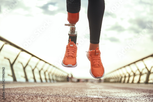 Never give up Cropped photo of disabled woman with prosthetic leg in sportswear jumping on the bridge