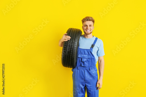 Young male mechanic with car tire on color background