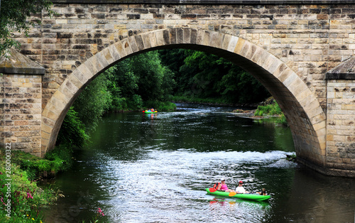 Ludzie w kajakach płyną rzeką pod starym mostem, spływ kajakowy.