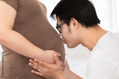 pregnant woman and her husband happy smiling while spending time together in the bedroom on white bed